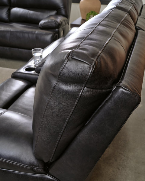 Close-up of a black leather recliner with a cup holder on a gray carpeted floor.